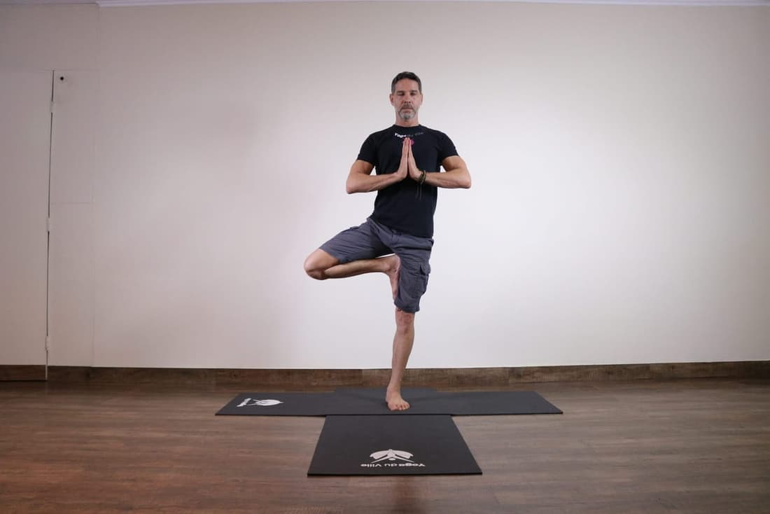 Instrutor Márcio demonstrando Vrikshasana, postura da árvore no yoga, em aula presencial no estúdio Yoga du Ville na Tijuca, RJ