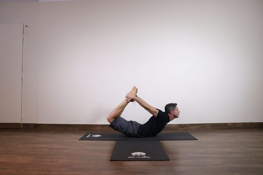 Homem praticando Dhanurasana, a postura do arco no yoga, com o corpo arqueado para trás