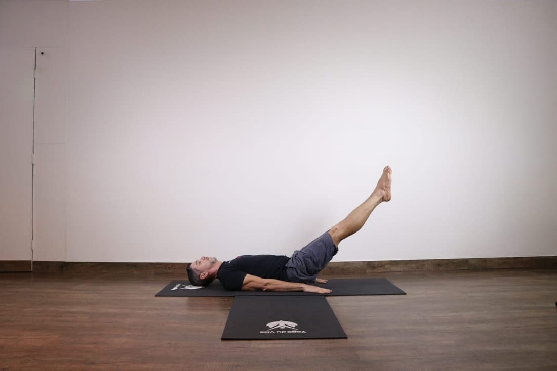 Homem praticando Uttanpadasana, postura da perna elevada no yoga, com as pernas inclinadas para cima