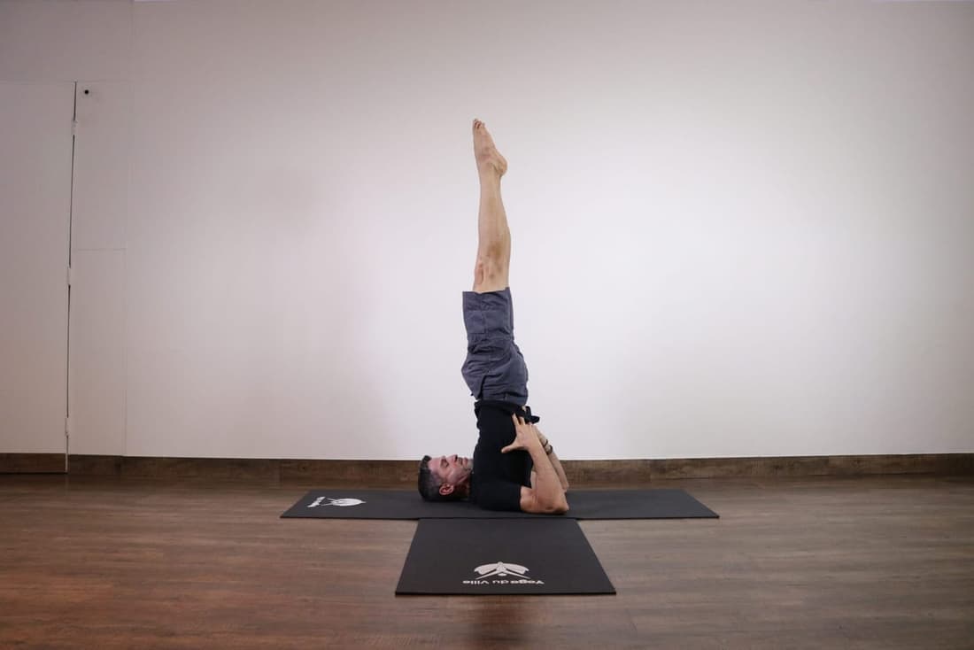 Instrutor Márcio executando Sarvangasana, postura da vela no yoga, durante aula no estúdio Yoga du Ville, Tijuca, RJ