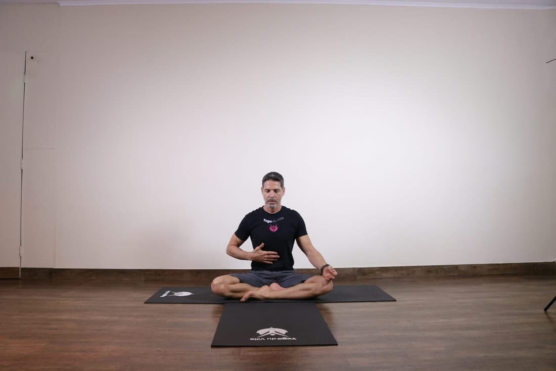 Homem sentado em posição de lótus praticando Kapalabhati Pranayama, técnica de respiração do fogo no yoga