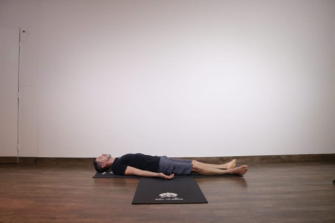 Homem deitado em Shavasana, postura do cadáver no yoga, com braços estendidos e olhos fechados