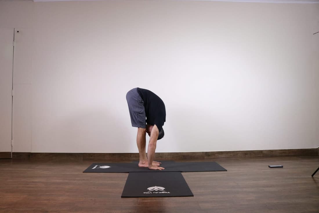 Homem praticando Uttanasana, postura de flexão para frente no yoga, com as mãos tocando o chão e o tronco colado às pernas