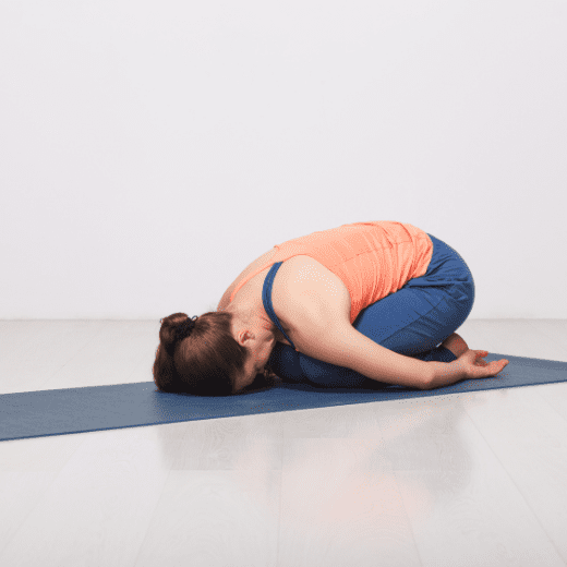 Mulher praticando Balasana, a postura da criança no yoga, ajoelhada e com a testa apoiada no tapete