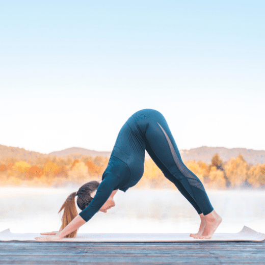 Mulher praticando Adho Mukha Svanasana, postura do cachorro olhando para baixo no yoga, com o corpo em forma de “V” invertido