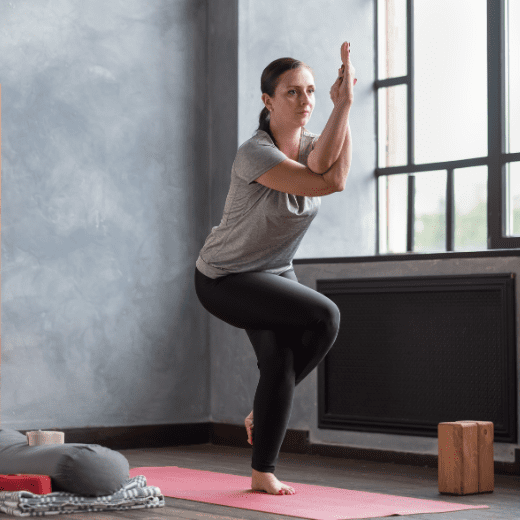Mulher praticando Garudasana, postura da águia no yoga, com pernas e braços entrelaçados em posição de equilíbrio