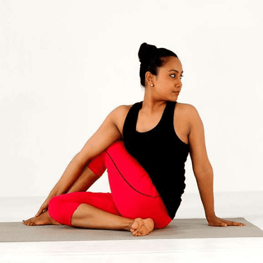 Mulher praticando Matsyendrasana, postura do senhor dos peixes no yoga, com o tronco torcido e mão apoiada no chão