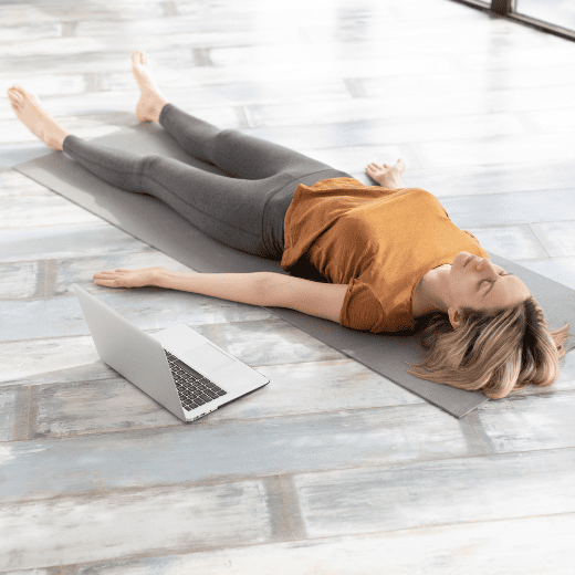 Mulher praticando Shavasana, postura do cadáver no yoga, deitada de costas com os braços relaxados ao lado do corpo