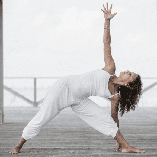 Mulher praticando Trikonasana, postura do triângulo no yoga, com uma mão no chão e outra estendida para o alto