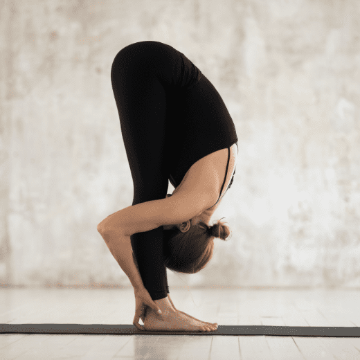 Mulher praticando Uttanasana, postura de flexão para frente no yoga, com a cabeça próxima aos joelhos