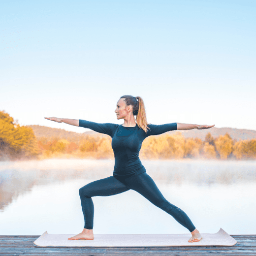 Mulher praticando Virabhadrasana, postura do guerreiro no yoga, com os braços estendidos e pernas firmes, em aula realizada na Tijuca, RJ.