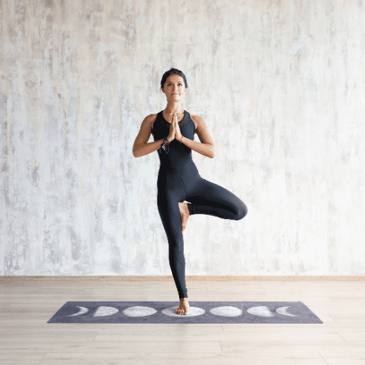 Mulher praticando Vrikshasana, postura da árvore no yoga, equilibrando-se em uma perna com mãos em prece, durante prática ao ar livre na Tijuca, RJ.