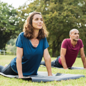 Casal praticando yoga ao ar livre na postura da cobra (Bhujangasana) sobre tapetes no parque