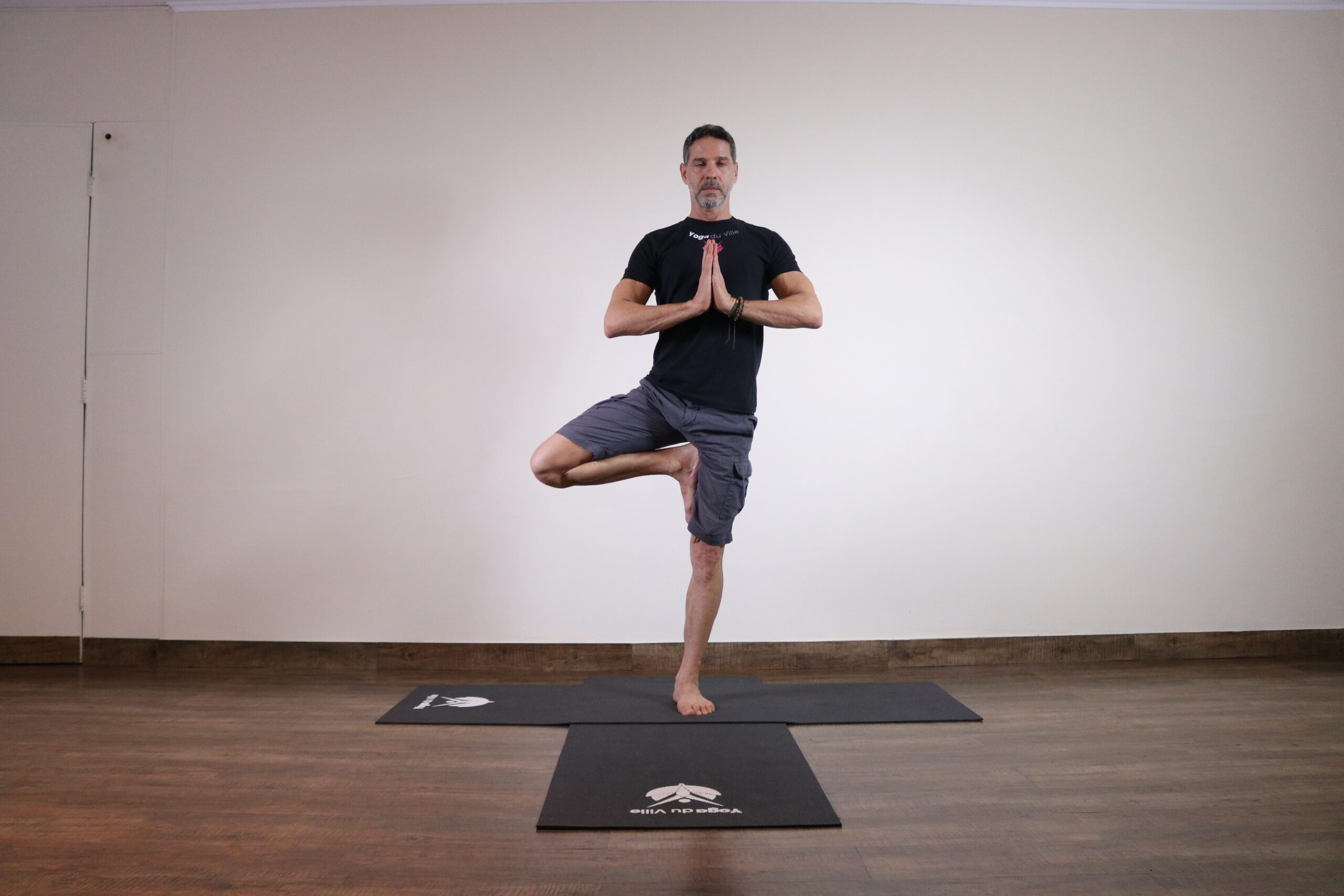 Instrutor Márcio demonstrando Vrikshasana, postura da árvore no yoga, em aula presencial no estúdio Yoga du Ville na Tijuca, RJ