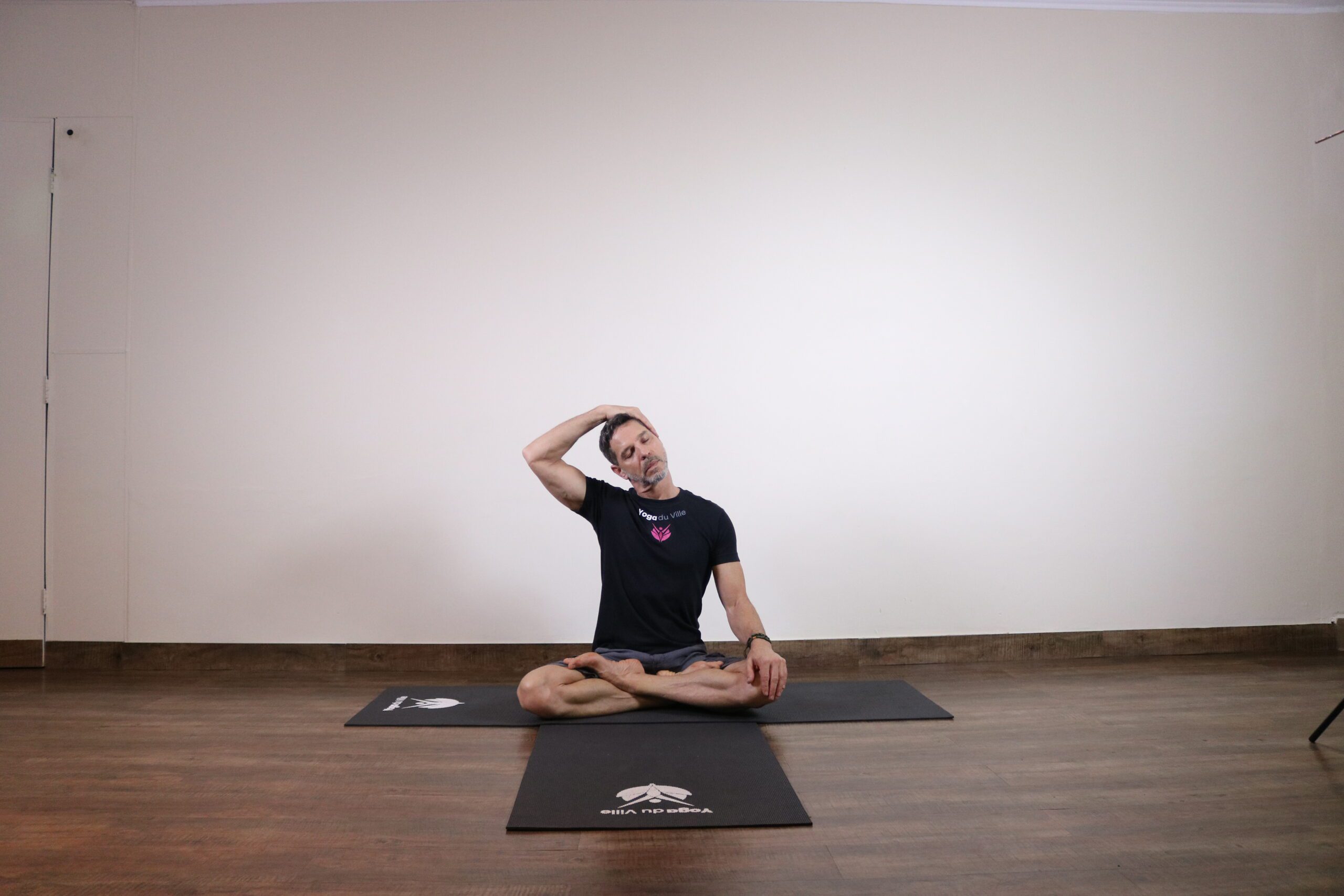 Instrutor Márcio realizando alongamento suave para o pescoço durante aula no estúdio Yoga du Ville, Tijuca, RJ
