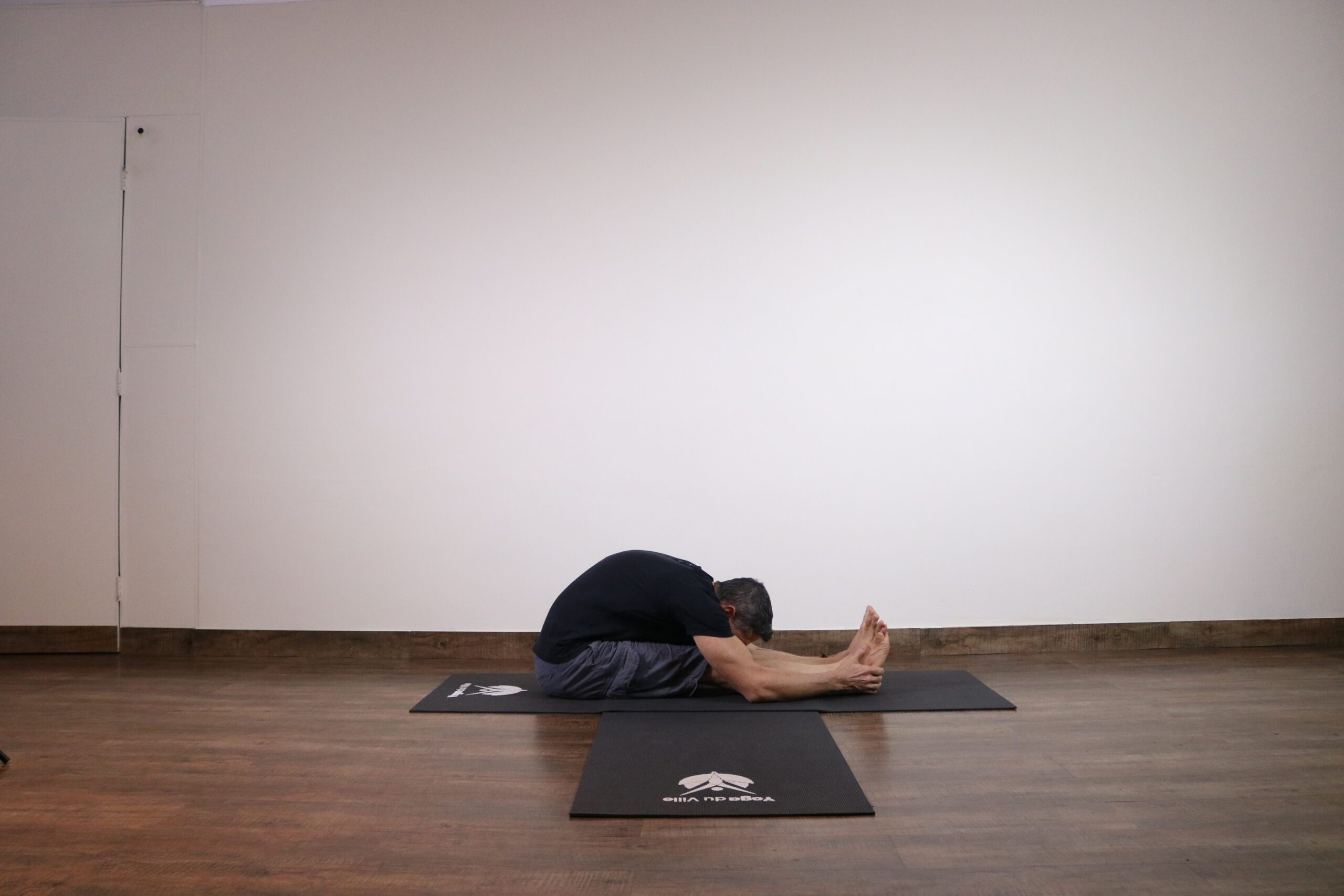 Professor Márcio demonstrando a postura Paschimottanasana (Pinça Sentada) durante aula de yoga na Tijuca, Rio de Janeiro.