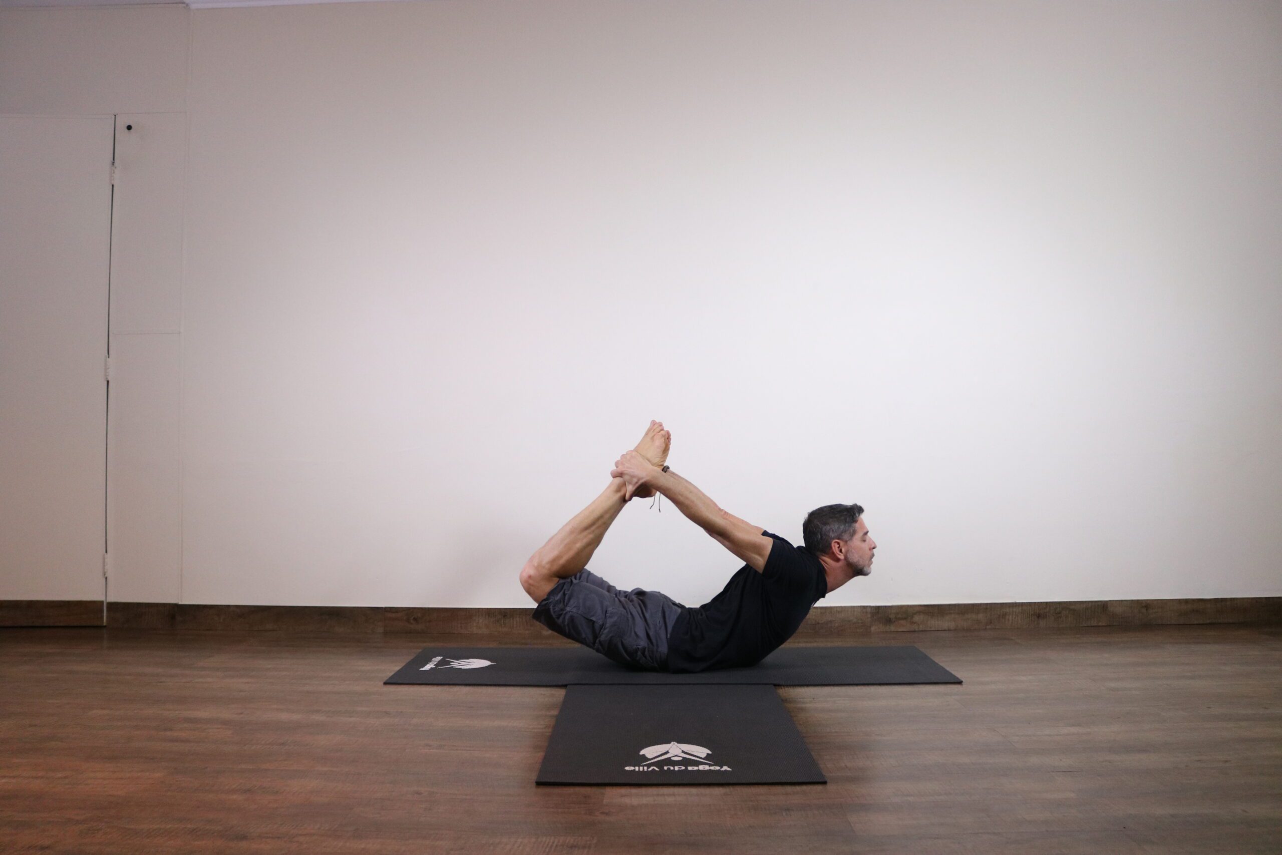Homem praticando Dhanurasana, a postura do arco no yoga, com o corpo arqueado para trás