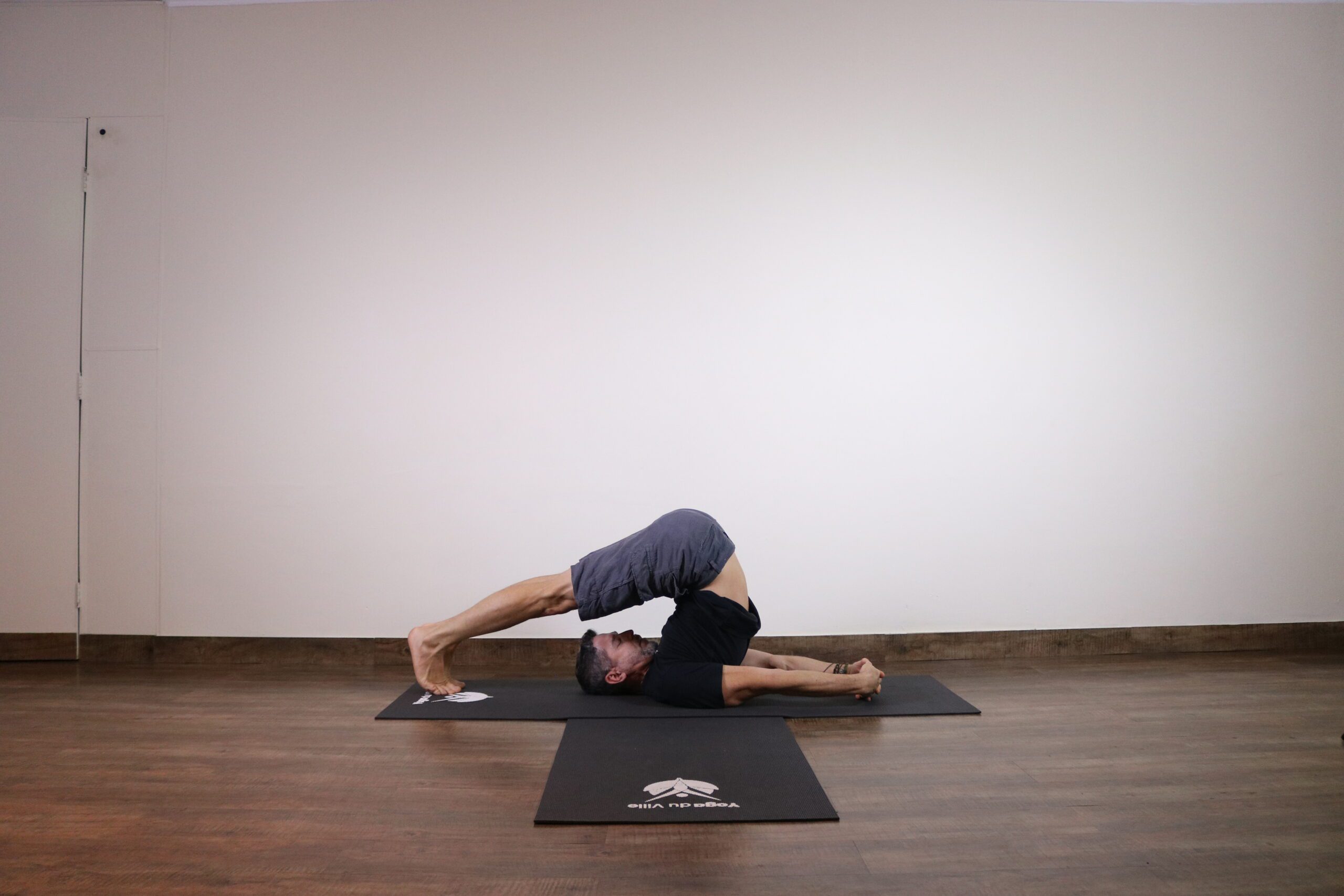 Homem executando Halasana, postura do arado no yoga, com pernas estendidas por trás da cabeça