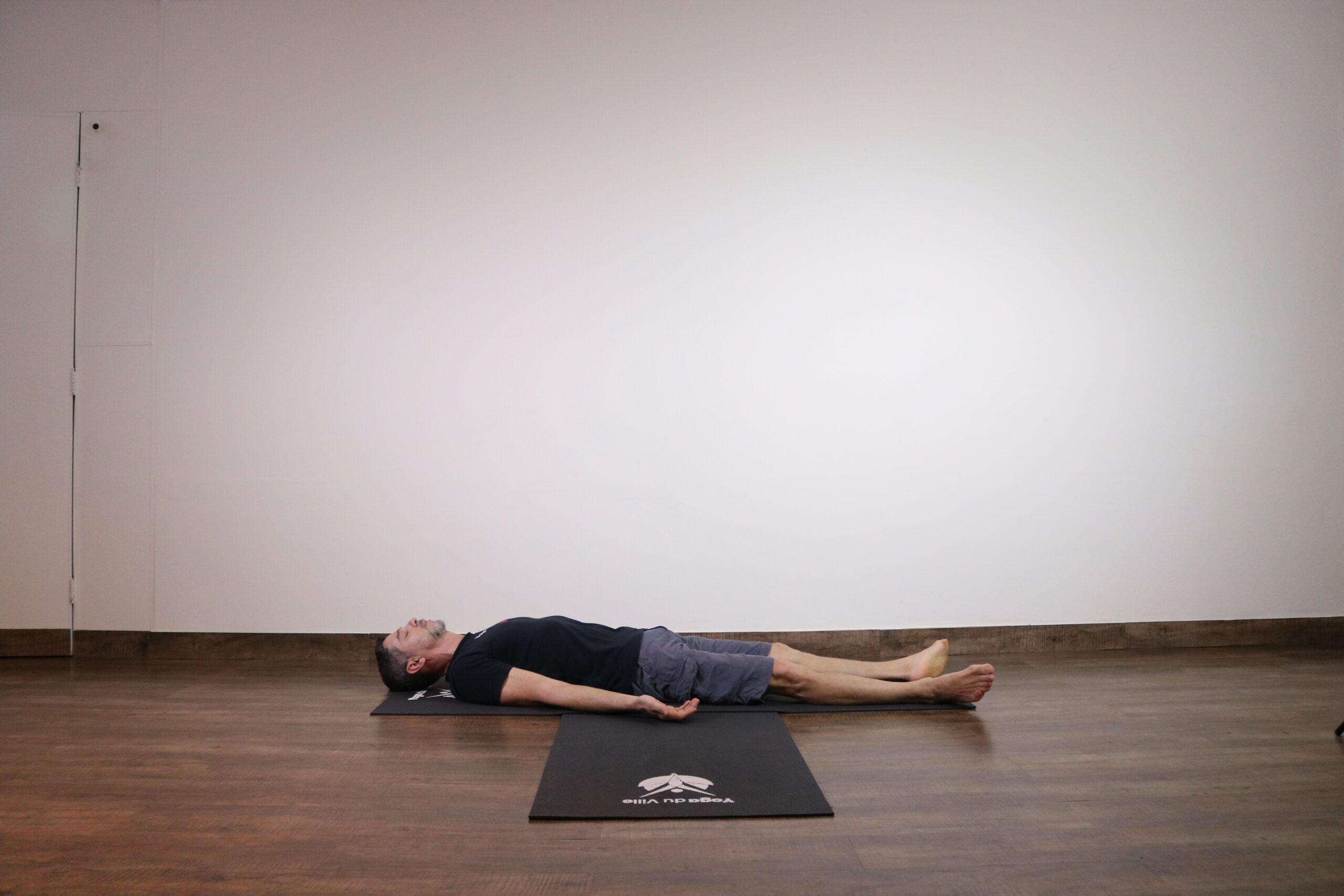 Homem deitado em Shavasana, postura do cadáver no yoga, com braços estendidos e olhos fechados