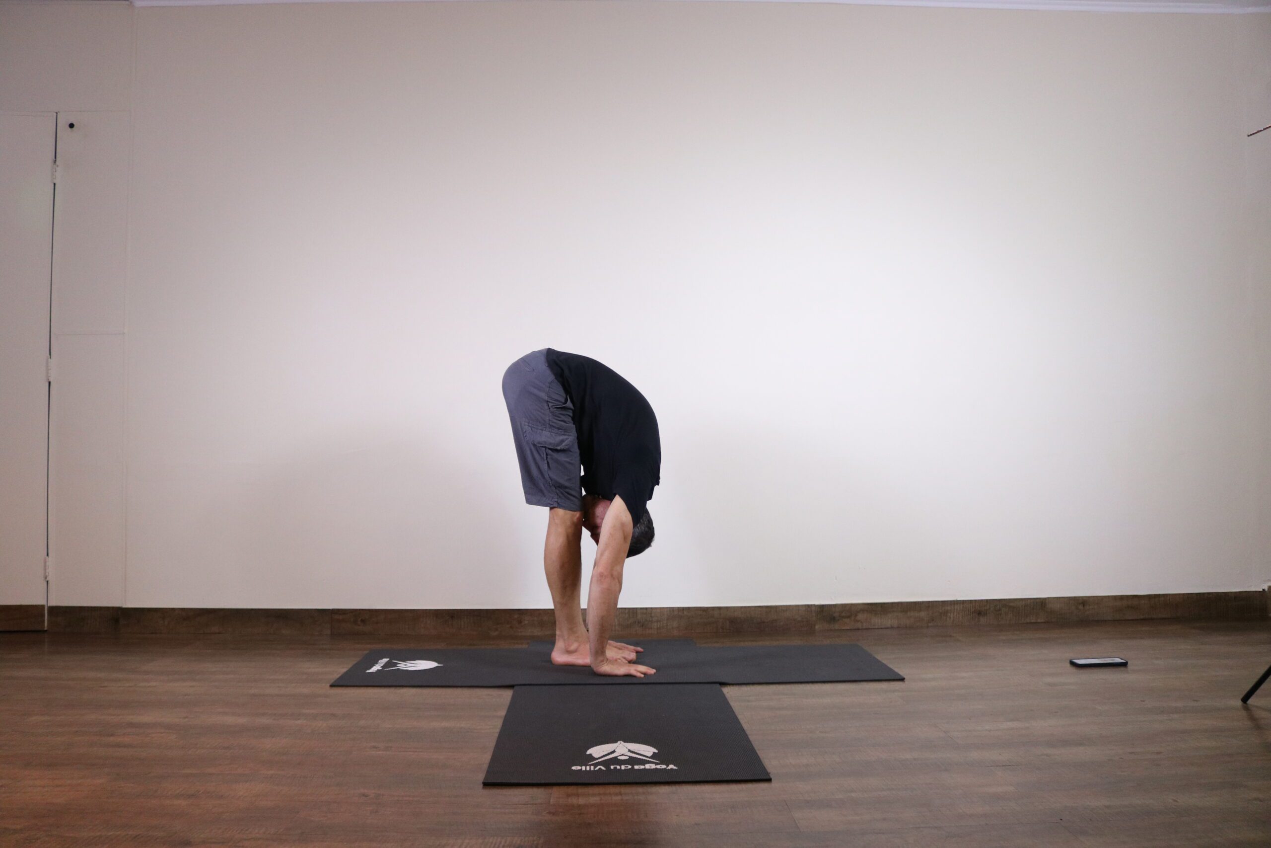 Homem praticando Uttanasana, postura de flexão para frente no yoga, com as mãos tocando o chão e o tronco colado às pernas