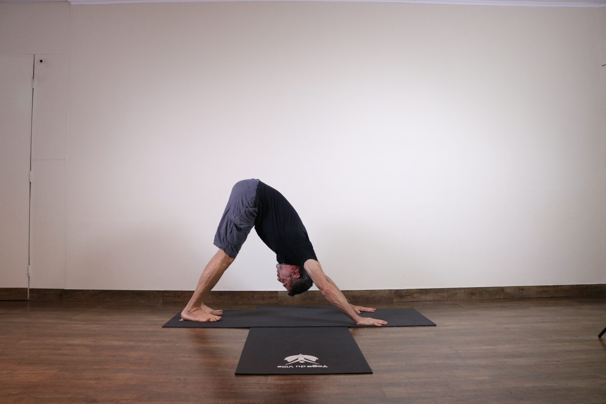 Instrutor Márcio praticando Adho Mukha Svanasana, postura do cachorro olhando para baixo, em aula no estúdio Yoga du Ville na Tijuca, RJ