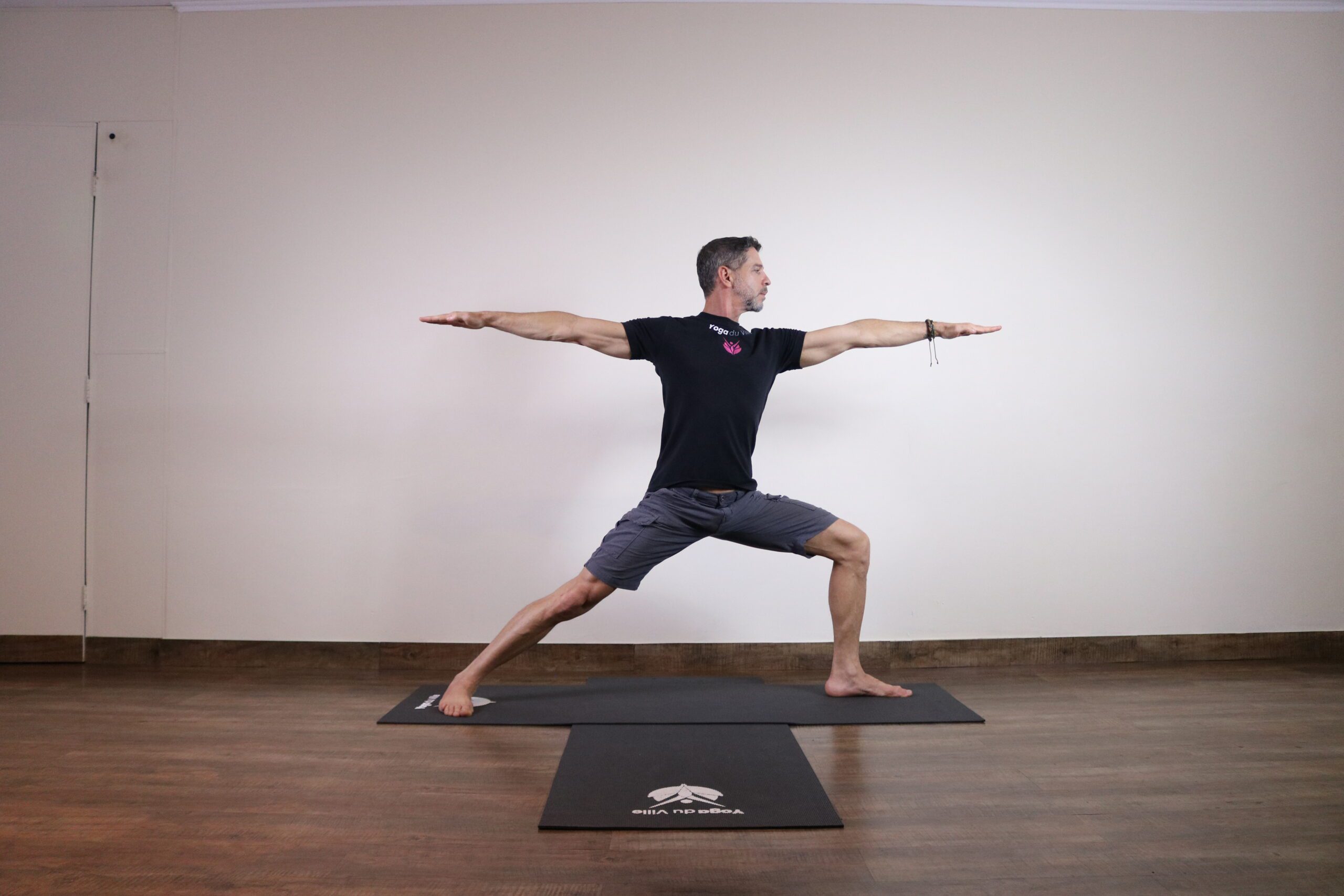Instrutor Márcio na postura Virabhadrasana II, Guerreiro 2 do yoga, em aula no estúdio Yoga du Ville, Tijuca, RJ